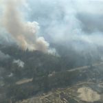 An aerial view of smoke rising from a wildfire burning through forest
